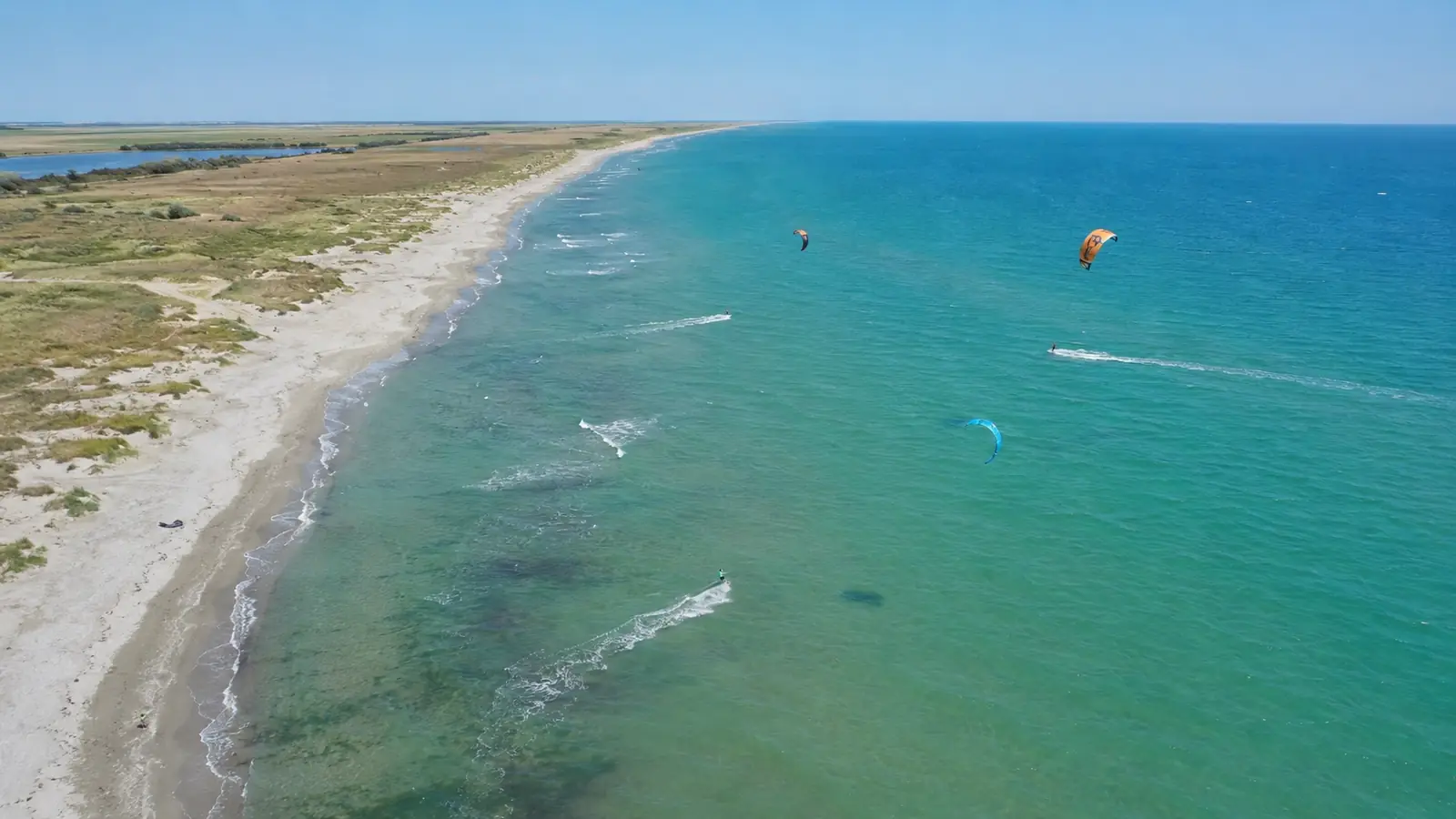 Vedere de sus asupra unei plaje sălbatice de pe litoralul românesc, cu mai mulți rideri de kitesurfing pe apă