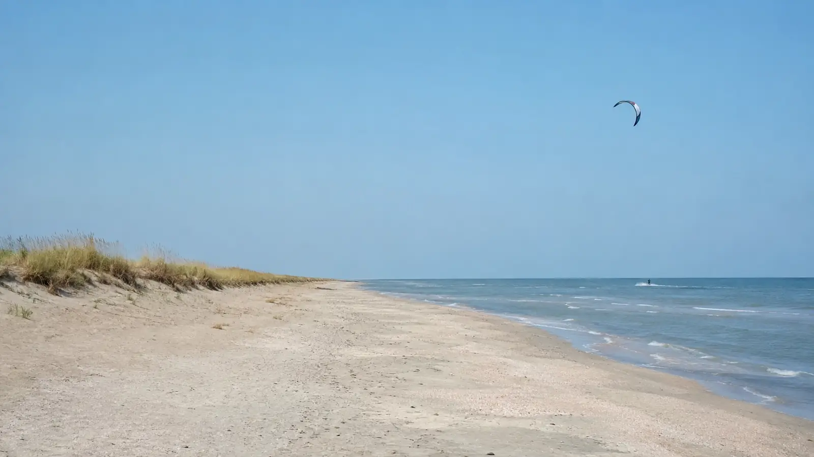 Plajă pustie cu dune pe litoralul nordic și un singur kite pe apă în depărtare